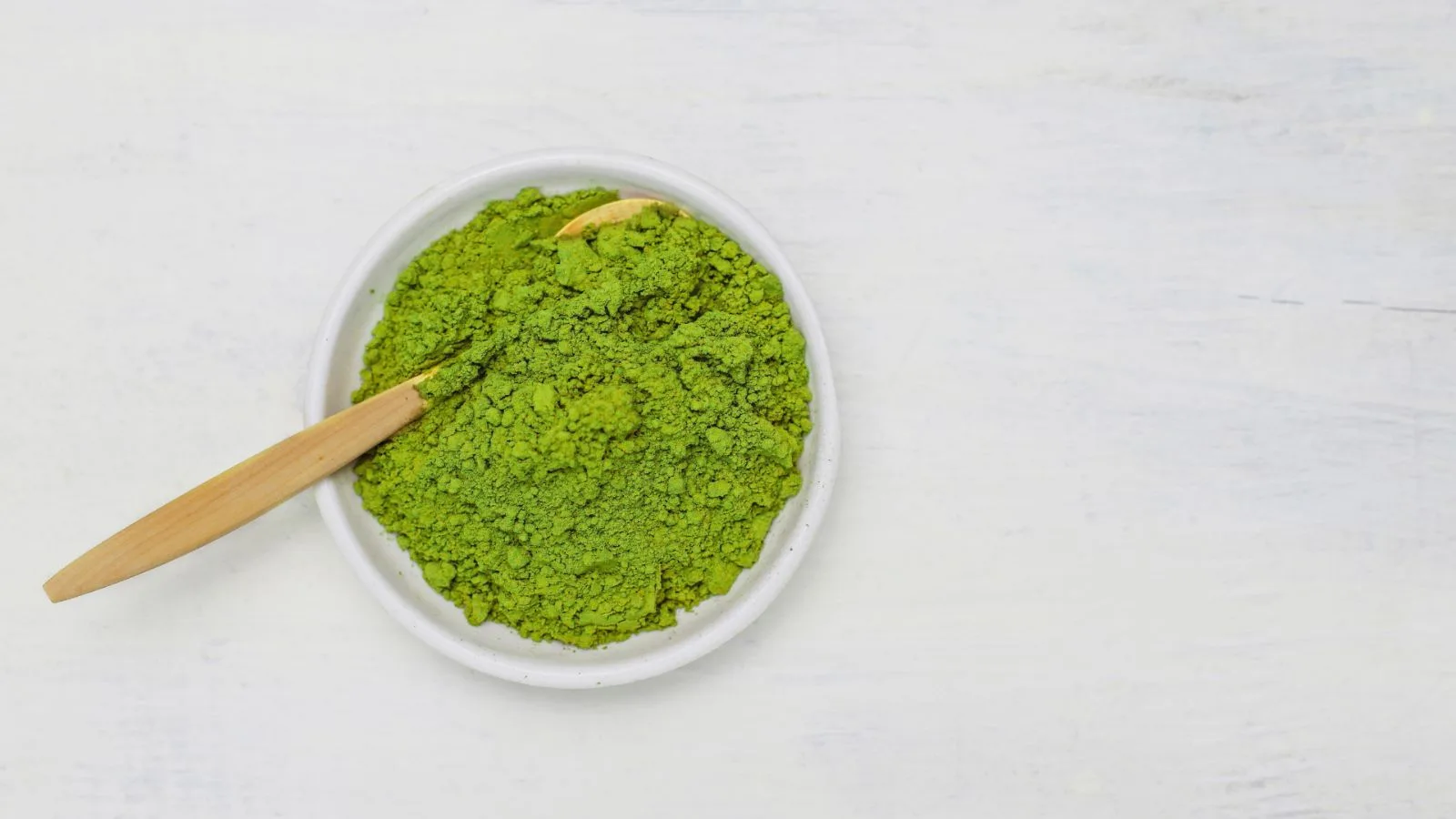 Bright green plant powder in a white ceramic dish with a wooden spoon